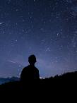 a silhouette of a person gazing up at a vast, star-filled night sky with shooting stars visible in the background