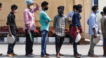 men wearing masks and waiting in line for food