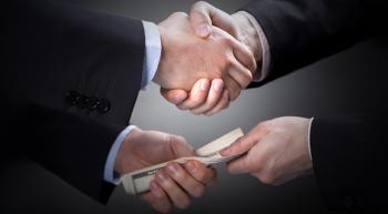Politicians shaking hands and slipping each other a bribe.