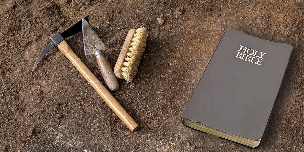 archaeological tools and a Bible laying on the dirt