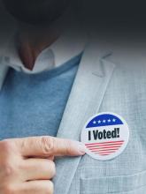 A man pointing proudly to a pin on his suit jacket that says, "I Voted!"