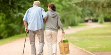 A woman helping an elderly man walk down a road